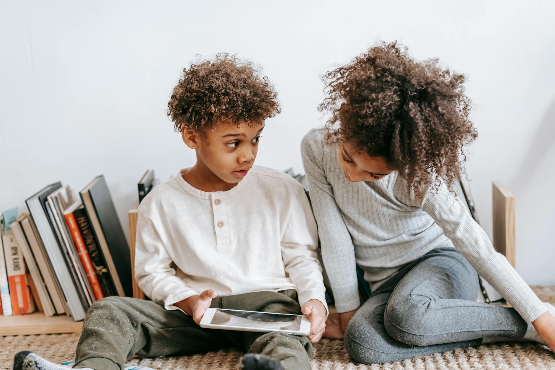 boy showing sister tablet screen in front of bookshelf
